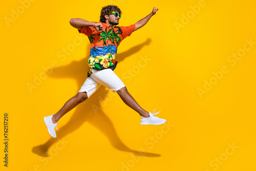 Full length photo of positive guy wear hawaii shirt in glasses jumping look at promo run empty space isolated on yellow color background