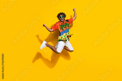 Full length photo of ecstatic guy wear hawaii shirt sneakers in glasses jumping shout yes win gambling isolated on yellow color background