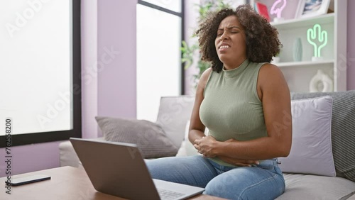 African american woman with abdominal pain sitting on sofa using laptop photo