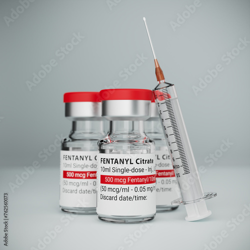 Three vials of the Fentanyl drug used as an analgesic but also source of the opioid crisis. A syringe leaning against the frontmost vial. Selective focus