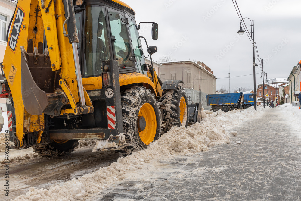 Clearing the street from snow in an urban environment. Snow plow tractor, bulldozer, excavator removes snow.