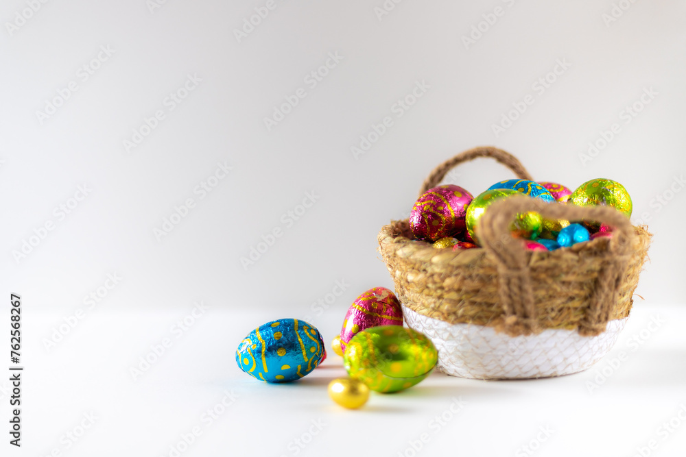 Easter eggs in basket with white background on white table. Studio lighting colorful easter decorated eggs for egg hunt with wicker basket and flowers. Banner for web and composition. Wishes card