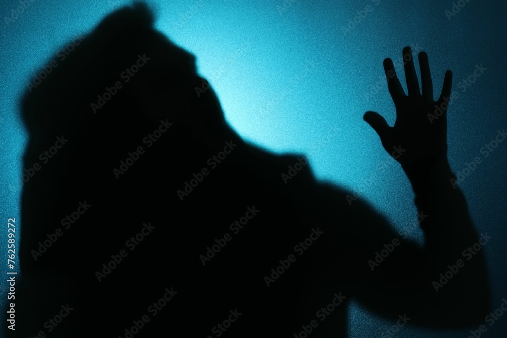 Silhouette of ghost behind glass against blue background