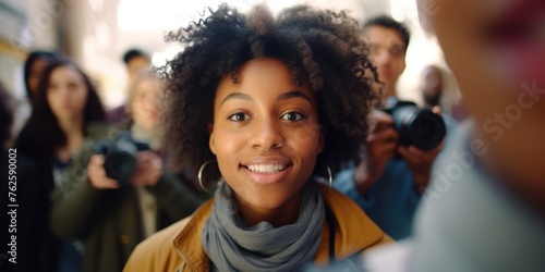 Woman with curly hair is smiling at camera. She is surrounded by people, some of whom are taking pictures of her