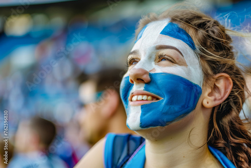 Happy Scottish female supporter with face painted in scotland flag which consists of a white saltire defacing a blue field, Scottish female fan at a sports event such as football or rugby match photo