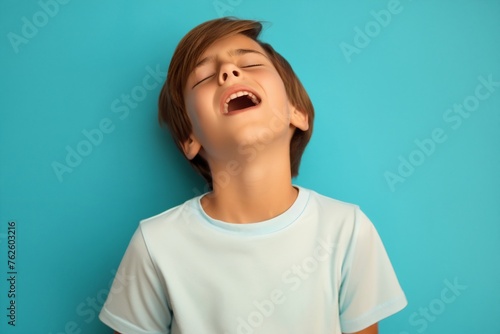Young boy standing in front of blue wall, looking up with closed eyes, surprised confusion, he heard or seen something unexpected or terrible. He very emotional expression sings songs
