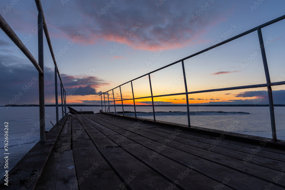 Abandoned broken pier is under sunset sky on a winter evening