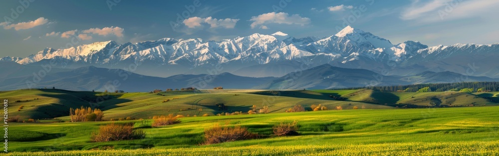 A green field stretches towards majestic mountains in the background under a clear blue sky.