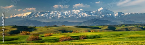 A green field stretches towards majestic mountains in the background under a clear blue sky.
