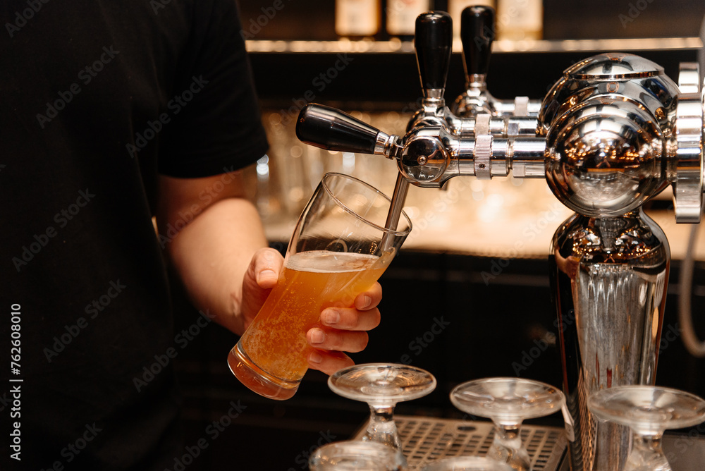 bartender pours light beer into large beer mug for customer at bar, close-up view of hand holding mug