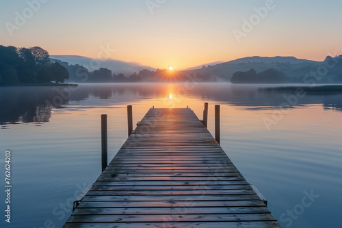 A beautiful sunrise over a calm lake, perfect for early morning exercise. Wooden dock extends into serene lake under the afterglow of a sunset