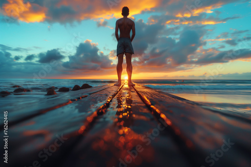 A person doing calisthenics exercises on a beach boardwalk at sunrise. Man gazes at ocean from pier at sunset, surrounded by water, sky, and afterglow