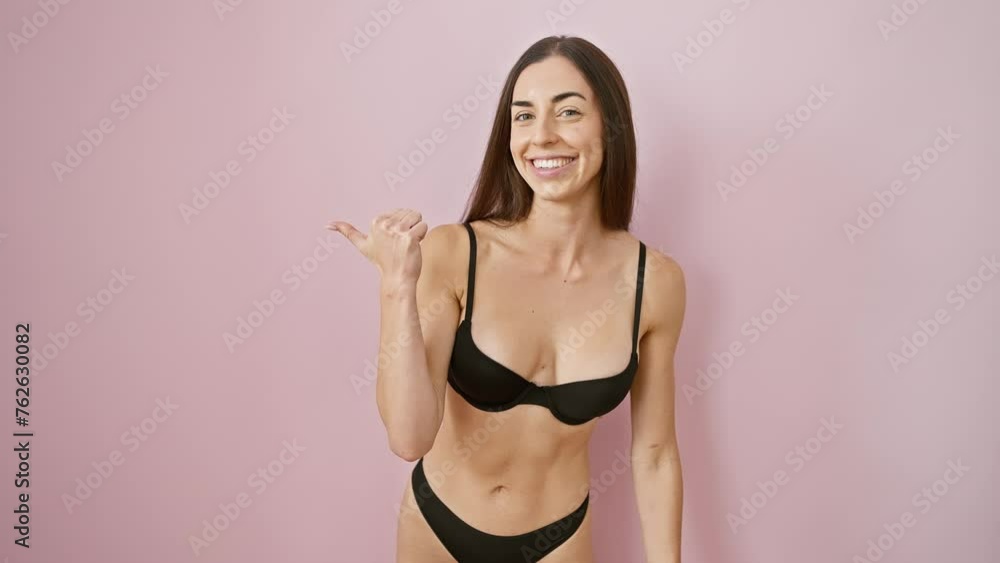 Bursting with joy, a young and beautiful hispanic woman in lovely lingerie happy points thumb on the side, smiling with open-mouthed cheer against a solo pink background Bursting with joy, a young and beautiful hispanic woman in lovely lingerie happy points thumb on the side, smiling with open-mouthed cheer against a solo pink background