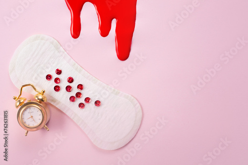 Blood, alarm clock and feminine hygiene pad with red glitter on pink background. First menstrual period concept photo