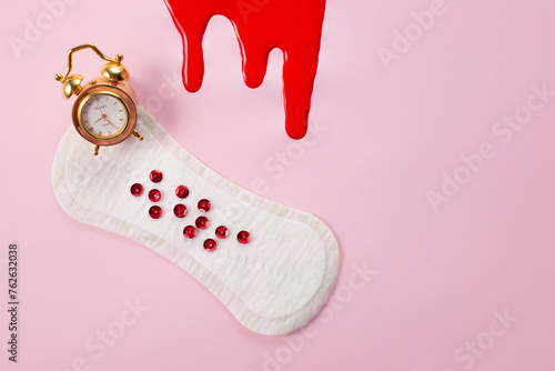 Blood, alarm clock and feminine hygiene pad with red glitter on pink background. First menstrual period concept photo