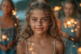 A joyful girl with sparkling blue eyes and freckles smiles brightly, surrounded by blurred figures with sparklers in a festive atmosphere.