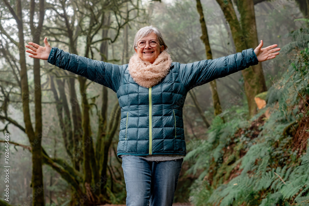 Happy senior woman with outstretched arms walks in the Garajonay national park in La Gomera. Elderly active woman hiking in mountain forest enjoying nature and healthy lifestyle
