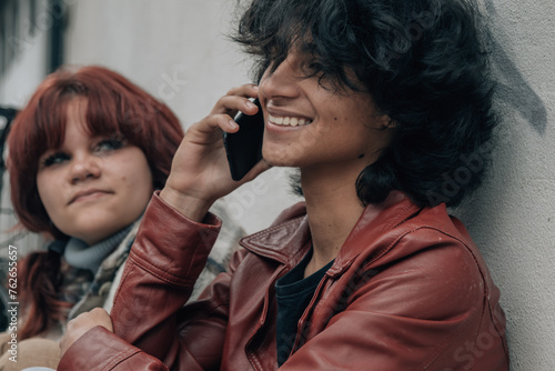 multiracial teenage couple sitting on the street talking on phone