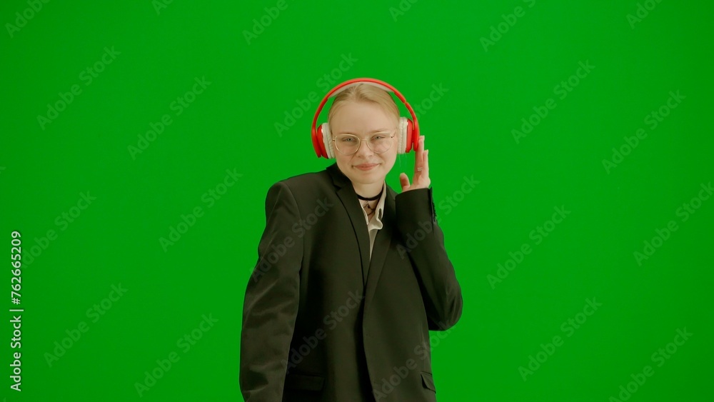 Portrait of female in suit on chroma key green screen. Blonde business woman in formal outfit walking in headphones listening music on smartphone. Front view. Portrait of female in suit on chroma key green screen. Blonde business woman in formal outfit walking in headphones listening music on smartphone. Front view.
