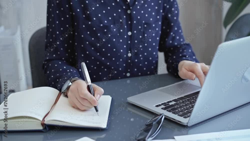 Businesswoman professional writing in a notebook beside a laptop at a modern workplace, close up view. Business concept Businesswoman professional writing in a notebook beside a laptop at a modern workplace, close up view. Business concept