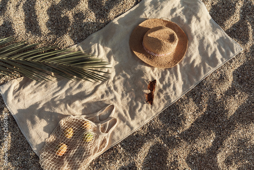 Straw hat, sunglasses, towel, bag on beach sand background. Aesthetic lifestyle, summer vacation concept. Sunbathing, beach party, picnic on summer holiday. Travel fashionable blog, social media.
