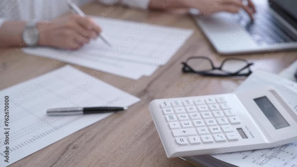 Close-up of a a calculator and documents on a wooden desk. Business professional working with papers and laptop on the background Close-up of a a calculator and documents on a wooden desk. Business professional working with papers and laptop on the background
