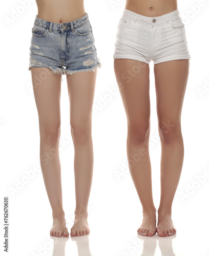 Close up photo of two barefoot women wearing short jeans on white studio background. Front view