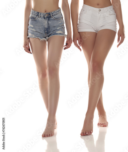 Close up photo of two barefoot women wearing short jeans on white studio background. Front view
