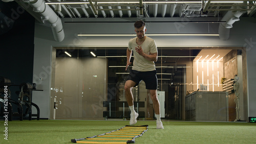 Caucasian sportsman man footballer soccer player training in sports gym exercise with ladder sport equipment workout cardio exercising jumping prepare for football match male athlete in fitness club photo