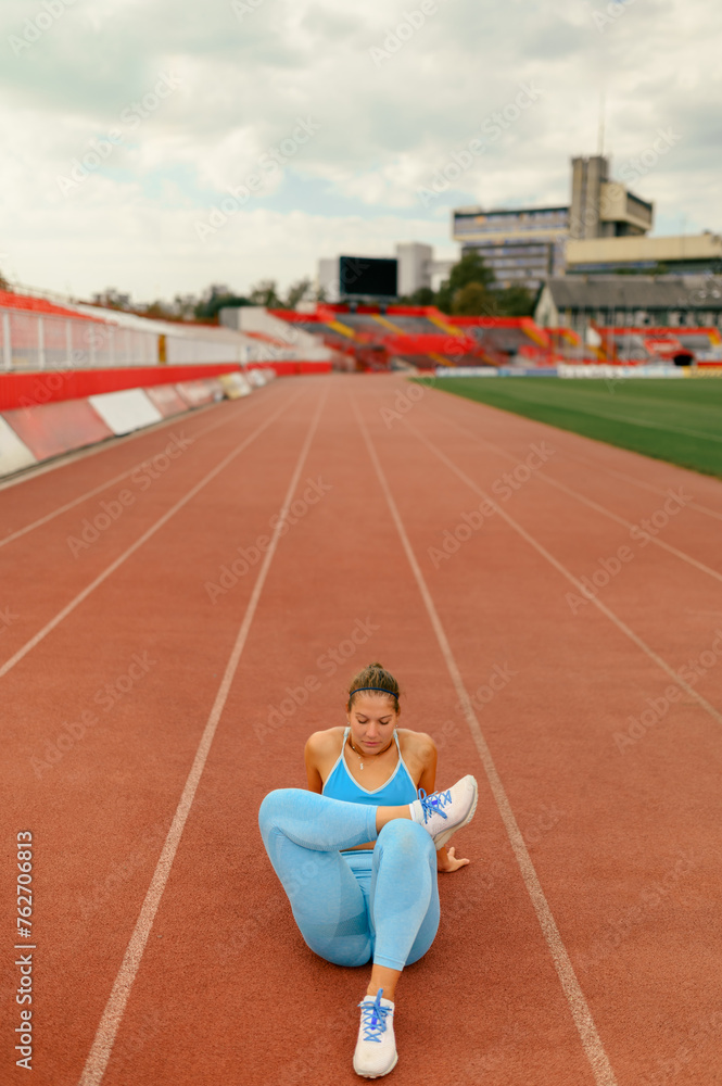 Woman sitting on a tartan racetrack and relaxing before or after sports training