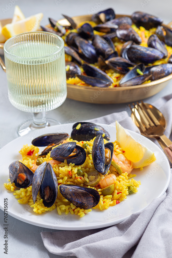 Seafood paella with mussels and shrimps, on white plate, served with lemon and white wine, vertical Seafood paella with mussels and shrimps, on white plate, served with lemon and white wine, vertical