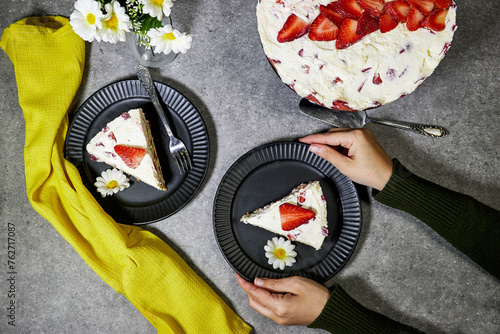 closeup hands holding a strawberry cake or Fraisier in french language in black plate on grunge gray background