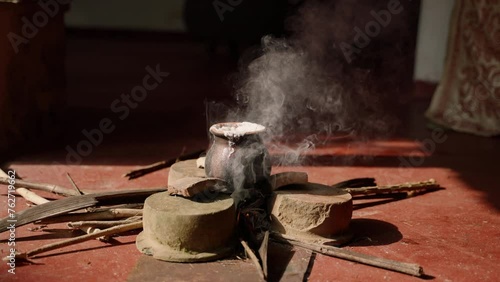 Clay pot with milk boiling over open fire, symbolizing prosperity in Sri Lankan Vesak celebrations. Smoke rises from ritual, sign of devotion and respect for Buddha Purnima traditions in home setting. photo