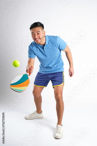 young asian man smiling in blue sportswear playing pickleball on white background © Alvaro