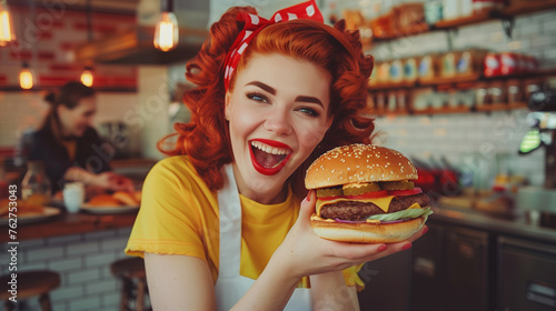 Beautiful waitress with red hair hold big burger posing and smiling in a restaurant against the background of the counter.