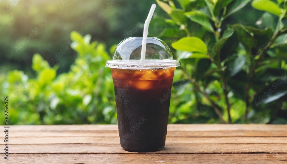 close up of take away plastic cup of iced black coffee americano on wooden table with garden green nature background close up of take away plastic cup of iced black coffee americano on wooden table with garden green nature background