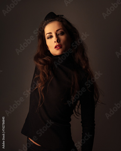 Beautiful makeup woman with red lipstick in black poloneck posing on dark shadow studio black background. Long brown hairstyle. Closeup