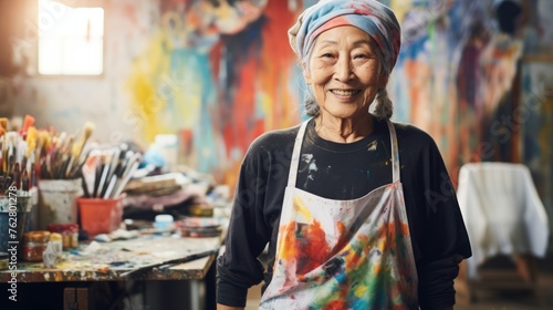 Elderly Asian lady artist next to her artwork in an art studio. Concept of artistic talent, senior creativity, art therapy, creative process, interesting hobby, exciting leisure time, oil painting