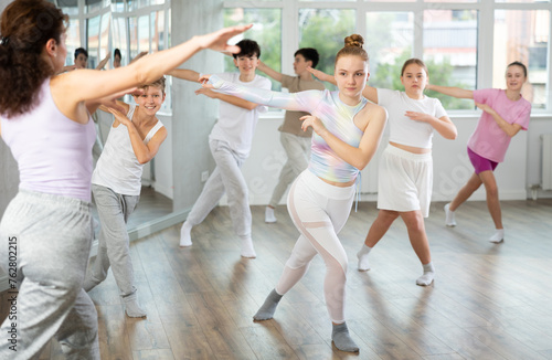 Girl teen performs modern dances repeats movements of unrecognizable teacher together with friends during lesson at choreographic school. Hobbies, active pastime
