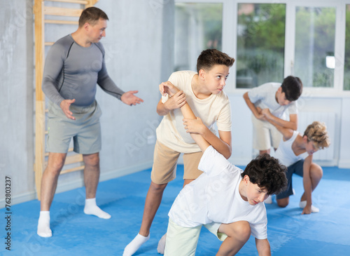 Boy doing strength painful hold while training self-defense in pairs with help of trainer in modern gym