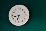 white traditional wall clock on a dark green interior wall