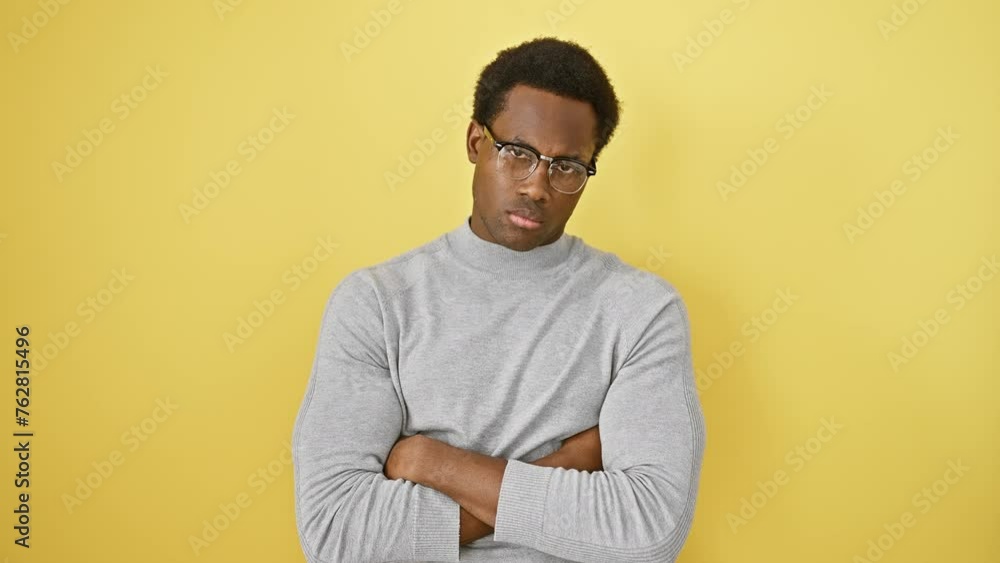Stressed out young african american man looking skeptic and displeased, crossing his arms in an upset stance, over a yellow isolated background. Stressed out young african american man looking skeptic and displeased, crossing his arms in an upset stance, over a yellow isolated background.