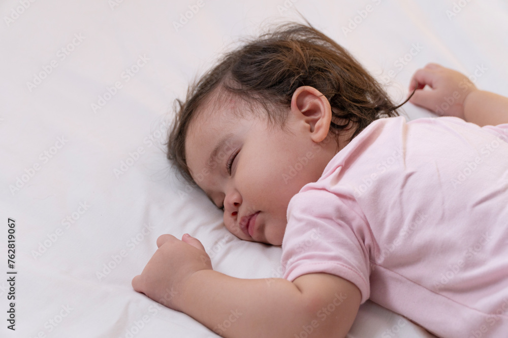 Healthy little baby girl infant wearing pink cloth sleeping calm peaceful relax on white bed at home. Adorable one year old toddler mixed race asleep having good dream resting in the bedroom.Lifestyle Healthy little baby girl infant wearing pink cloth sleeping calm peaceful relax on white bed at home. Adorable one year old toddler mixed race asleep having good dream resting in the bedroom.Lifestyle