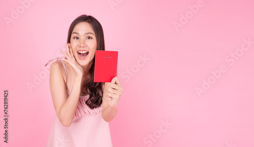 Excited asian traveller woman showing red passport plan vacation holiday toothy smile standing over isolated pink background. Happy young girl pink dresses holding hand beside mouth excited journey.