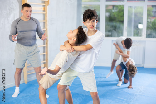 Determined teenagers sparring at self-defense training, trying to break free of back grab. Boys practicing basic techniques under guidance of experience instructor....