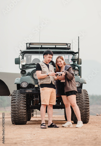 Young couple stands together outdoors, sharing a moment over a vintage camera with a car in the background.