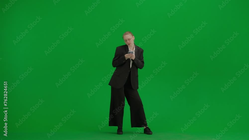 Portrait of female in suit on chroma key green screen. Blonde business woman in formal outfit holding smartphone and dancing, texting in app. Portrait of female in suit on chroma key green screen. Blonde business woman in formal outfit holding smartphone and dancing, texting in app.