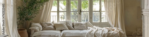 A room with a white sofa with pillows and blankets against the backdrop of a large window.