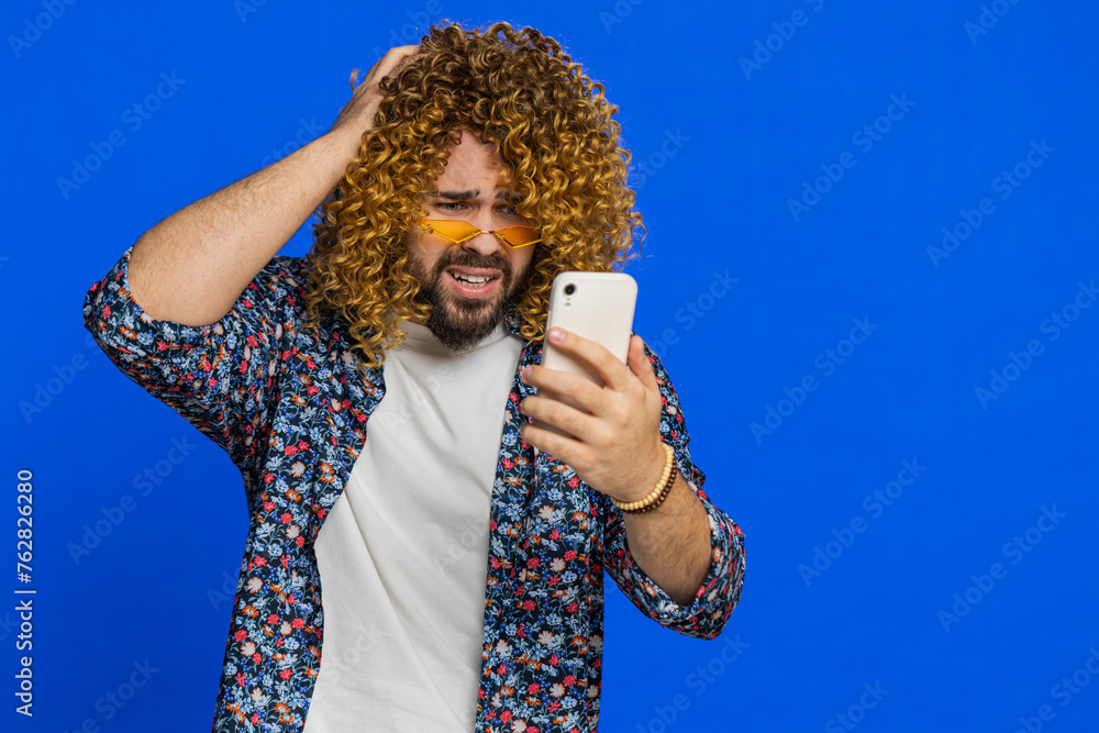 Φωτογραφία Upset sad man with curly hairstyle wig use smartphone typing browsing play game loses surprised by sudden lottery results bad fortune loss fail unlucky news