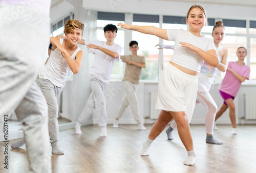 Female girl student repeats movements of unrecognizable teacher during group modern dance class. Hobbies, active pastime, additional extracurricular activities for children and teenagers